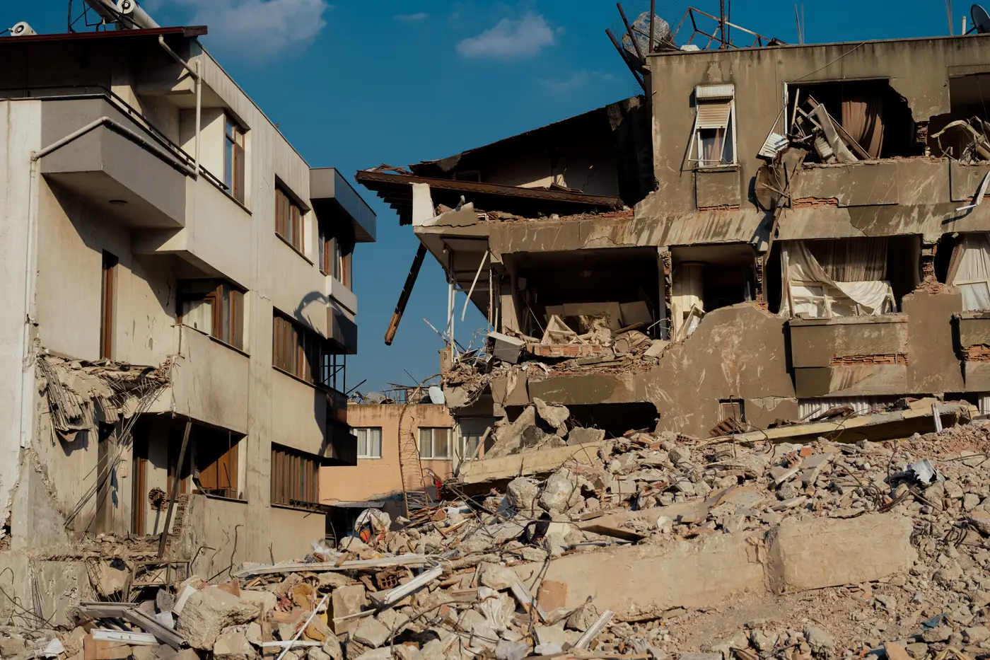 A multi-story apartment building with its floors collapsed and stacked on each other after an earthquake, rubble piled below.